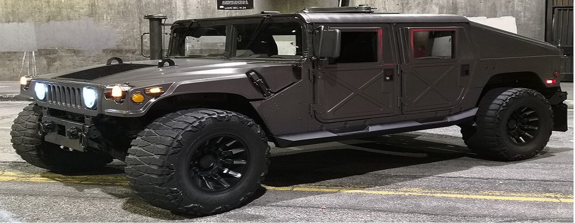 Armor-plated HMMWV with door hardware visible, staged in a fabrication bay