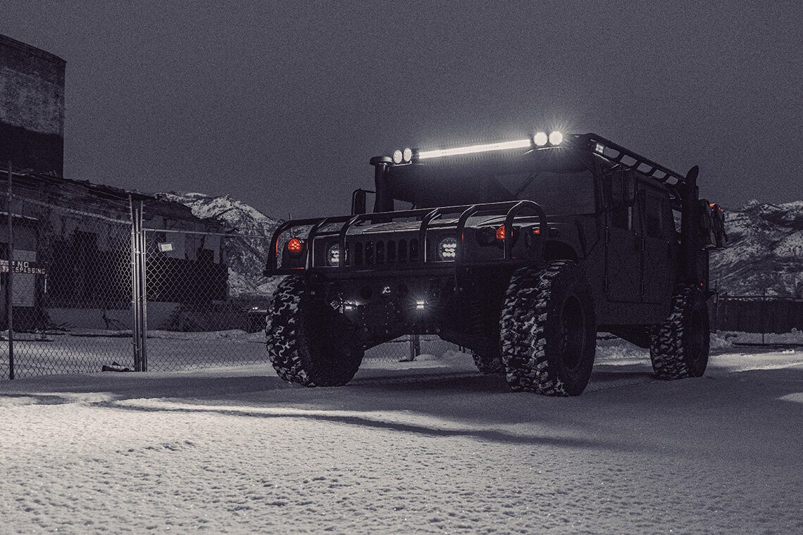 Blacked-out ruggedized HMMWV build with a roof light bar, photographed at night in snow