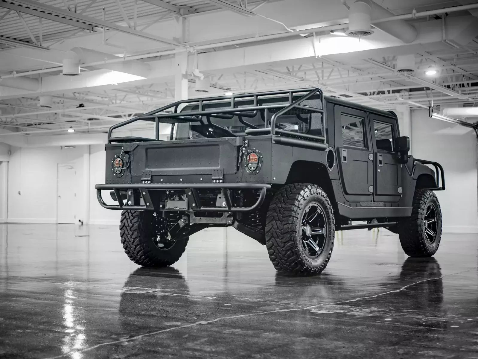 Open-top HMMWV build with a full roll cage, photographed in a white industrial space
